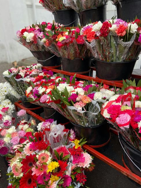 A vibrant display of freshly arranged flower bouquets featuring a variety of blooms such as pink and white carnations, red gerbera daisies, yellow daisies, and pink chrysanthemums, all wrapped in clea