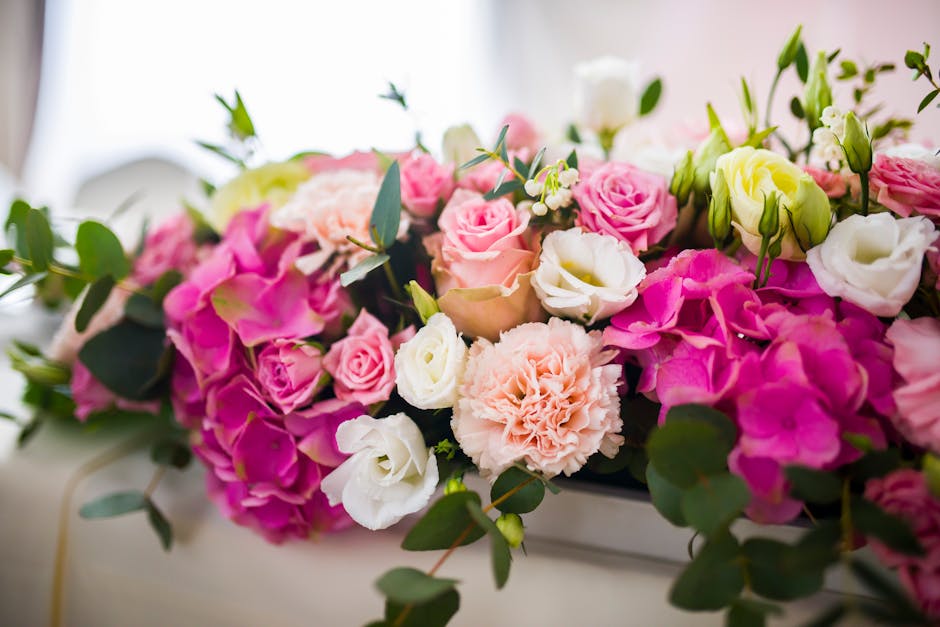 A lush floral arrangement featuring a variety of fresh flowers including pink and white roses, light pink carnations, and pale yellow lisianthus, accented with green eucalyptus leaves. The flowers are